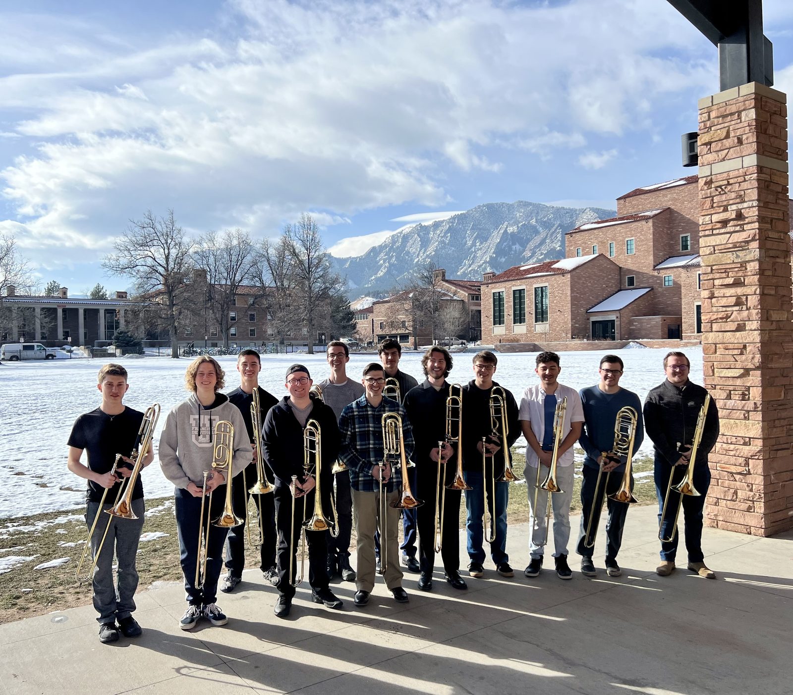 The University of Colorado Boulder Trombone Choir standing outside on campus with the Flatirons behind them